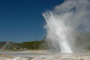 Daisy Geyser erupting with visitors visible in the distance..  Daisy Geyser, a cone-type geyser that shoots out of the ground diagonally, is predictable with intervals ranging from 120 to over 200 minutes.  It reaches heights of 75 feet, lasts 3 to 4 minutes and rarely erupts in concert with nearby Splendid Geyser.  Upper Geyser Basin, Yellowstone National Park, Wyoming