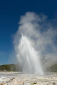 Daisy Geyser erupting with visitors visible in the distance..  Daisy Geyser, a cone-type geyser that shoots out of the ground diagonally, is predictable with intervals ranging from 120 to over 200 minutes.  It reaches heights of 75 feet, lasts 3 to 4 minutes and rarely erupts in concert with nearby Splendid Geyser.  Upper Geyser Basin, Yellowstone National Park, Wyoming