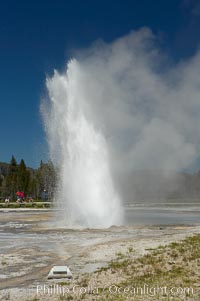 Daisy Geyser erupting with visitors visible in the distance..  Daisy Geyser, a cone-type geyser that shoots out of the ground diagonally, is predictable with intervals ranging from 120 to over 200 minutes.  It reaches heights of 75 feet, lasts 3 to 4 minutes and rarely erupts in concert with nearby Splendid Geyser.  Upper Geyser Basin, Yellowstone National Park, Wyoming