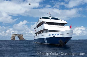 Sky Dancer, a liveaboard dive tour boat, at anchor near Darwin Island with Darwins Arch in the background