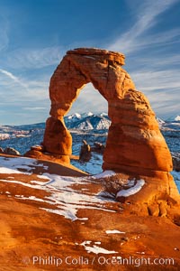 Delicate Arch, dusted with snow, at sunset, with the snow-covered La Sal mountains in the distance.  Delicate Arch stands 45 feet high, with a span of 33 feet, atop of bowl of slickrock sandstone, Arches National Park, Utah