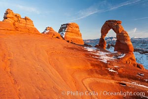 Delicate Arch, dusted with snow, at sunset, with the snow-covered La Sal mountains in the distance.  Delicate Arch stands 45 feet high, with a span of 33 feet, atop of bowl of slickrock sandstone, Arches National Park, Utah