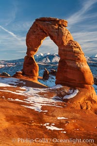 Delicate Arch, dusted with snow, at sunset, with the snow-covered La Sal mountains in the distance.  Delicate Arch stands 45 feet high, with a span of 33 feet, atop of bowl of slickrock sandstone, Arches National Park, Utah