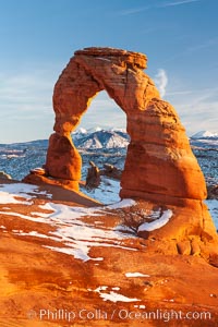 Delicate Arch, dusted with snow, at sunset, with the snow-covered La Sal mountains in the distance.  Delicate Arch stands 45 feet high, with a span of 33 feet, atop of bowl of slickrock sandstone, Arches National Park, Utah