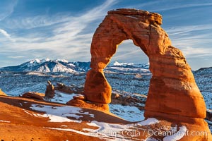 Delicate Arch, dusted with snow, at sunset, with the snow-covered La Sal mountains in the distance.  Delicate Arch stands 45 feet high, with a span of 33 feet, atop of bowl of slickrock sandstone.