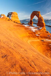 Delicate Arch, dusted with snow, at sunset, with the snow-covered La Sal mountains in the distance.  Delicate Arch stands 45 feet high, with a span of 33 feet, atop of bowl of slickrock sandstone, Arches National Park, Utah