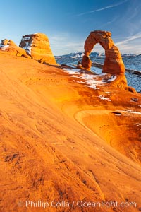 Delicate Arch, dusted with snow, at sunset, with the snow-covered La Sal mountains in the distance.  Delicate Arch stands 45 feet high, with a span of 33 feet, atop of bowl of slickrock sandstone, Arches National Park, Utah