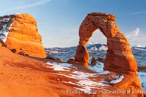 Delicate Arch, dusted with snow, at sunset, with the snow-covered La Sal mountains in the distance.  Delicate Arch stands 45 feet high, with a span of 33 feet, atop of bowl of slickrock sandstone, Arches National Park, Utah