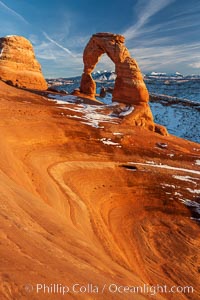 Delicate Arch, dusted with snow, at sunset, with the snow-covered La Sal mountains in the distance.  Delicate Arch stands 45 feet high, with a span of 33 feet, atop of bowl of slickrock sandstone, Arches National Park, Utah