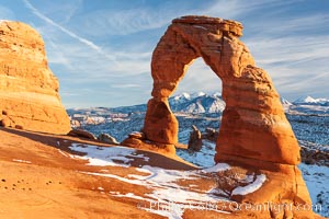 Delicate Arch, dusted with snow, at sunset, with the snow-covered La Sal mountains in the distance.  Delicate Arch stands 45 feet high, with a span of 33 feet, atop of bowl of slickrock sandstone, Arches National Park, Utah