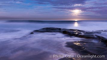 Breaking waves crash upon a rocky reef under the light of a full moon, La Jolla, California