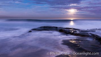 Breaking waves crash upon a rocky reef under the light of a full moon.