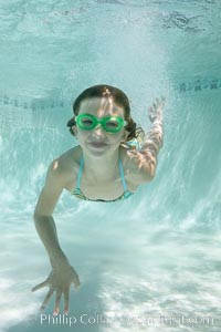A young girl swimming with goggles in a bright swimming pool