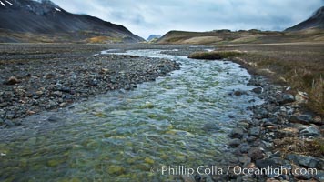 Glacial melt waters, runoff, flows across an alluvial flood plain between mountains, on its way to Stromness Bay.