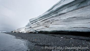 Horizontal striations and layers in packed snow, melting and overhanging, seen from the edge of the snowpack, along a rocky beach, Brown Bluff