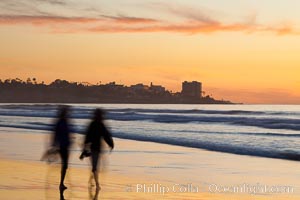 Tourists walk along La Jolla Shores beach at sunset.  Point La Jolla is visible in the distance, Scripps Institution of Oceanography