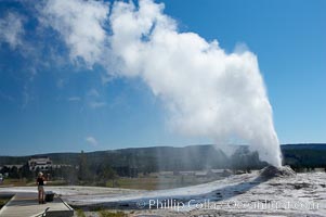 A visitor videotapes the eruption of Lion Geyser, with Old Faithful Inn visible in the distance.  Lion Geyser, whose eruption is preceded by a release of steam that sounds like a lion roaring, erupts just once or a few times each day, reaching heights of up to 90 feet.  Upper Geyser Basin, Yellowstone National Park, Wyoming