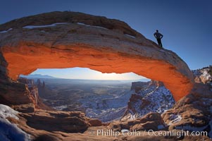 Mesa Arch, spectacular stone arch overlooking Canyonlands National Park.  An hiker watches the dawning sun from atop Mesa Arch, Island in the Sky