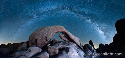 The Milky Way galaxy arcs above Arch Rock, panoramic photograph, cylindrical projection, Joshua Tree National Park, California