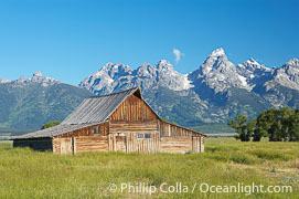 An old barn at Mormon Row is lit by the morning sun with the Teton Range rising in the distance.