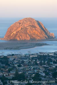 Morro Rock lit at sunrise, rises above Morro Bay which is still in early morning shadow