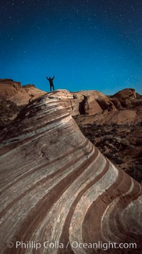 Exuberant hiker atop the Fire Wave, at night, stars and the evening sky.