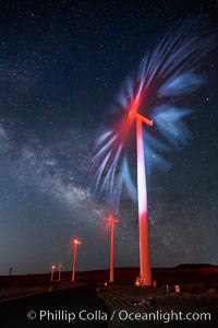 Ocotillo Wind Energy Turbines, at night with stars and the Milky Way in the sky above, the moving turbine blades illuminated by a small flashlight.