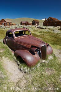 Old car lying in dirt field, Fuller Street and Green Street buildings in background, Bodie State Historical Park, California