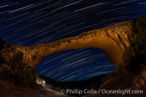 Owachomo Bridge and Star Trails, at night.  Owachomo Bridge, a natural stone bridge standing 106' high and spanning 130' wide,stretches across a canyon with the Milky Way crossing the night sky.