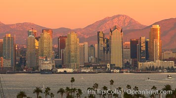 San Diego city skyline, showing the buildings of downtown San Diego rising above San Diego Harbor, viewed from Point Loma at sunset, with mountains of the Cleveland National Forest rising in the distance