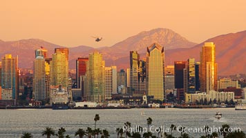 San Diego city skyline, showing the buildings of downtown San Diego rising above San Diego Harbor, viewed from Point Loma at sunset, with mountains of the Cleveland National Forest rising in the distance. Lyons Peak is in center and the flanks of Mount San Miguel to the right