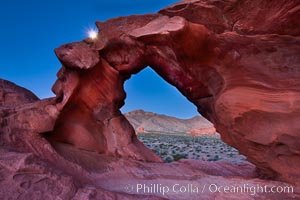 Natural arch formed in sandstone frames the setting moon, Valley of Fire State Park