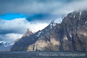 South Georgia Island coastline, showing the island's characteristic rugged topography.  56% of the island is covered by 161 glaciers, which have created numerous large bays and inlets that provide excellent habitat for marine animals and seabirds. Mountains meet the sea in steep-sided seacliffs covered with sparse vegetation.  The highest point on South Georgia Island is Mt. Paget at 2,915m