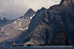 South Georgia Island coastline, showing the island's characteristic rugged topography.  56% of the island is covered by 161 glaciers, which have created numerous large bays and inlets that provide excellent habitat for marine animals and seabirds. Mountains meet the sea in steep-sided seacliffs covered with sparse vegetation.  The highest point on South Georgia Island is Mt. Paget at 2,915m