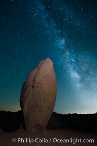 Standing stone and Milky Way, stars fill the night sky.