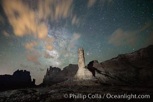 Stone columns rising in the night sky, milky way and stars and clouds filling the night sky overhead. (Note: this image was created before a ban on light-painting in Arches National Park was put into effect.  Light-painting is no longer permitted in Arches National Park)