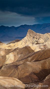 Sunrise at Zabriskie Point, Manly Beacon is lit by the morning sun while dark clouds lie on the horizon, Death Valley National Park, California