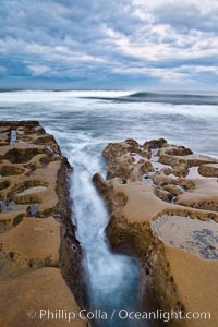 Waves wash over sandstone reef, clouds and sky.