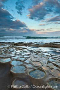 Waves wash over sandstone reef, clouds and sky.