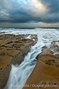 Waves wash over sandstone reef, clouds and sky, La Jolla, California