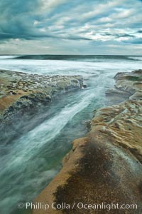 Waves wash over sandstone reef, clouds and sky, La Jolla, California