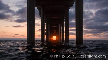 Scripps Pier solstice, surfer's view from among the waves, sunset aligned perfectly with the pier. Research pier at Scripps Institution of Oceanography SIO, sunset, La Jolla, California