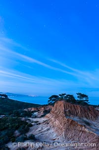 Torrey Pines State Reserve at Night, stars and clouds fill the night sky with the lights of La Jolla visible in the distance, San Diego, California