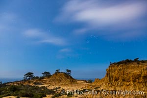 Torrey Pines State Reserve at Night, stars and clouds fill the night sky with the lights of La Jolla visible in the distance, San Diego, California