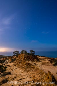 Torrey Pines State Reserve at Night, stars and clouds fill the night sky with the lights of La Jolla visible in the distance, San Diego, California