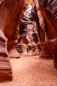 A hiker admiring the striated walls and dramatic light within Antelope Canyon, a deep narrow slot canyon formed by water and wind erosion.
