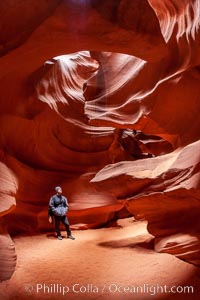 Image 17995, A hiker admiring the striated walls and dramatic light within Antelope Canyon, a deep narrow slot canyon formed by water and wind erosion. Navajo Tribal Lands, Page, Arizona, USA, Phillip Colla, all rights reserved worldwide. Keywords: adventure, antelope canyon, arizona, backpacking, camping, canyon, desert, environment, erosion, explore, geologic features, geology, gulch, hiker, hiking, landscape, narrow, nature, navaho, navajo tribal lands, page, ravine, sandstone, slot, slot canyon, trail, tribal, upper antelope canyon, usa.