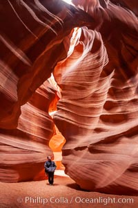 A hiker admiring the striated walls and dramatic light within Antelope Canyon, a deep narrow slot canyon formed by water and wind erosion, Navajo Tribal Lands, Page, Arizona