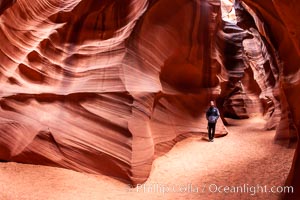 A hiker admiring the striated walls and dramatic light within Antelope Canyon, a deep narrow slot canyon formed by water and wind erosion, Navajo Tribal Lands, Page, Arizona