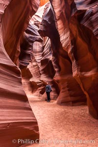 A hiker admiring the striated walls and dramatic light within Antelope Canyon, a deep narrow slot canyon formed by water and wind erosion, Navajo Tribal Lands, Page, Arizona